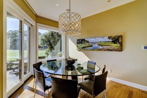 Un comedor con mesa y sillas de vidrio, una lámpara colgante y un cuadro de un paisaje en la pared.