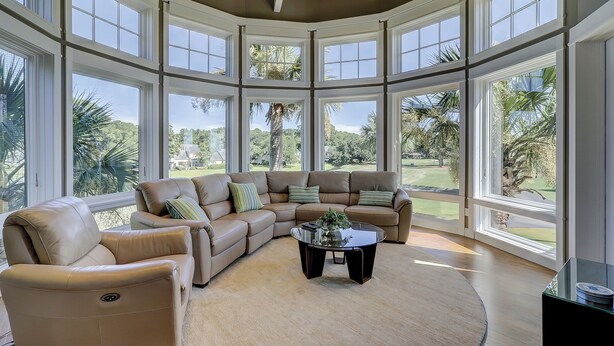 A spacious living room with a large sectional sofa, a round coffee table, and a view of a golf course through large windows. - 38 Windjammer Court at The Sea Pines Resort (Hilton Head Island)