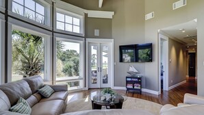 A spacious living room with a leather sofa, a glass coffee table, and a TV mounted on the wall. - 38 Windjammer Court at The Sea Pines Resort (Hilton Head Island)