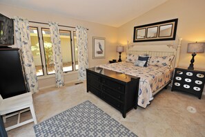 Un dormitorio con cama, cómoda, televisor y ventana con cortinas.