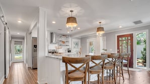 A modern kitchen with white cabinetry, wooden chairs, and pendant lighting. - 43 Stoney Creek at The Sea Pines Resort (Hilton Head Island)