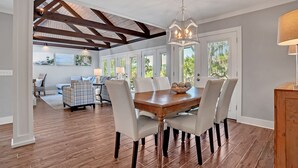 A dining area with a wooden table and chairs, a chandelier, and a view of the outdoors through large windows. - 43 Stoney Creek at The Sea Pines Resort (Hilton Head Island)
