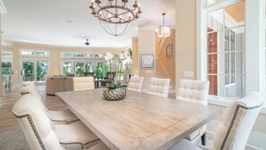 Een ruime eethoek met een houten tafel, wit beklede stoelen en een kroonluchter.