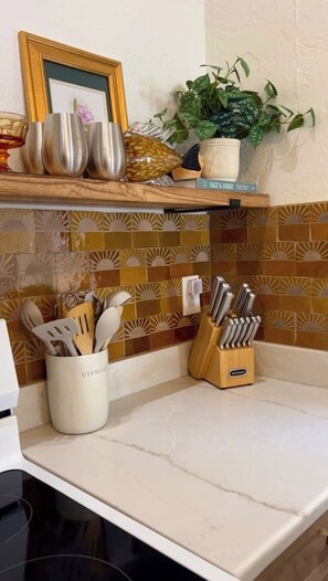 A kitchen with a white countertop, a utensil holder, a knife block, and a potted plant on a shelf.