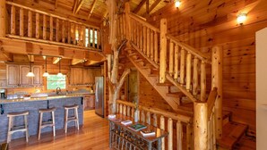 A wooden cabin interior with a kitchen, bar area, and a staircase.