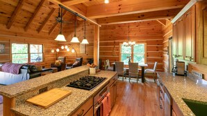 A spacious log cabin interior with a kitchen island, dining area, and seating.