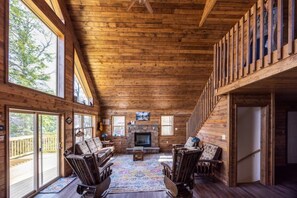 A spacious wooden interior with a fireplace, large windows, and a balcony.