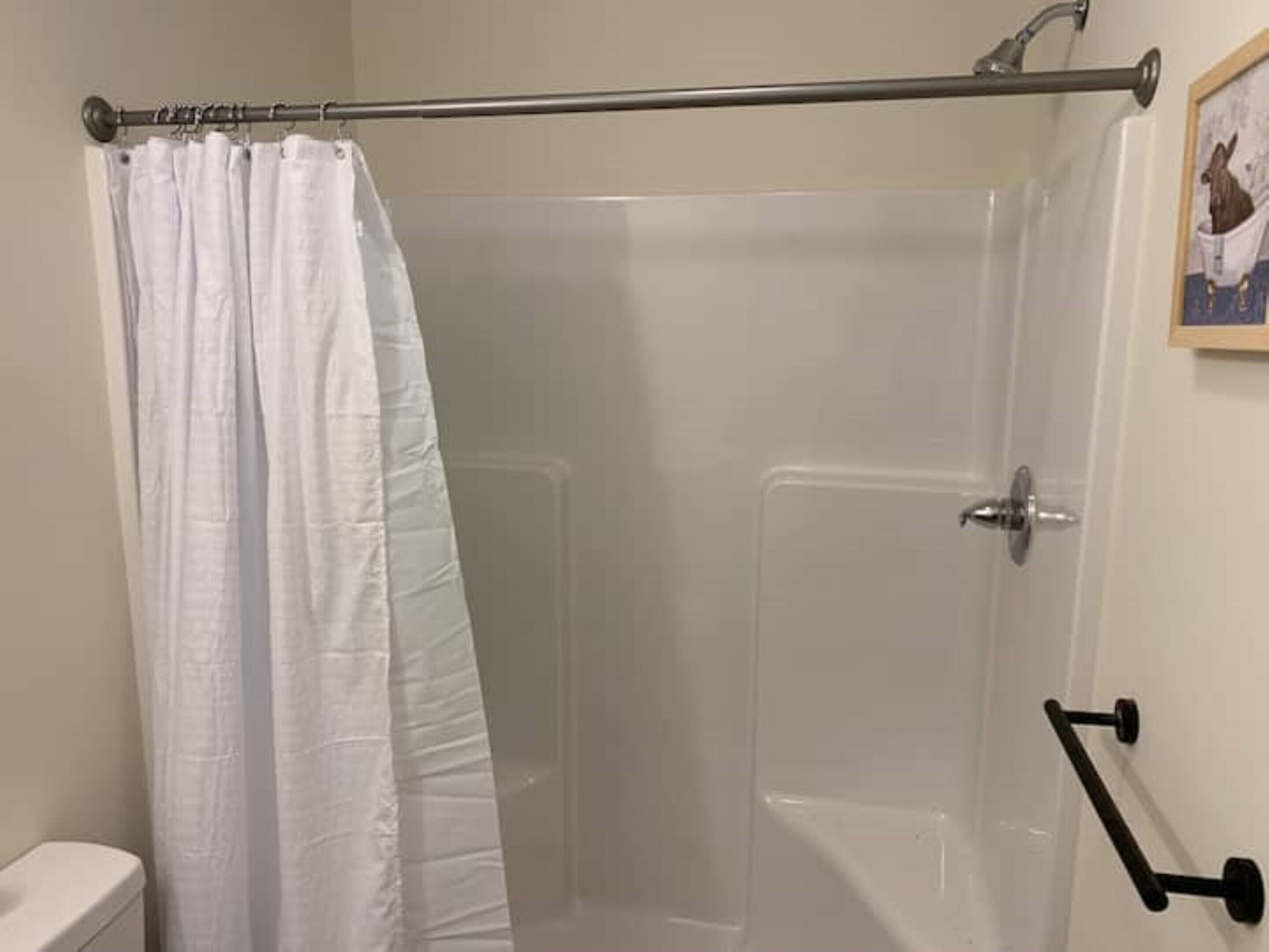 Et bruseområde med hvidt badeforhæng, glasdør og gelænder.