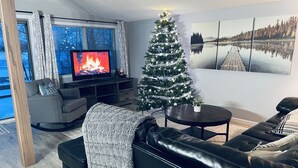 Een woonkamer met een open haard, kerstboom, bank en televisie.