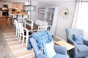 A modern kitchen with white cabinetry, a dining area with white chairs, and a blue armchair with a pillow. - Lake Escape with paddle boards, fire pit & game room (Lake Park)