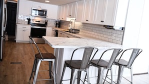 Een moderne keuken met witte kasten, een marmeren eiland en barkrukken.