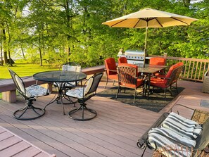A deck with a round table and chairs, a grill, and a large umbrella. - Lake Escape | paddle boards, fire pit & game room (Lake Park)
