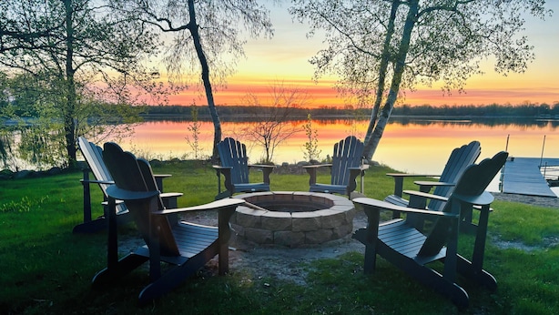 Een zitgedeelte aan het meer met Adirondack-stoelen en een vuurkorf van steen.