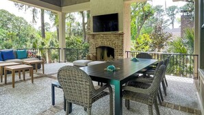 An outdoor patio with a brick fireplace, wicker furniture, and a TV mounted above the fireplace. - 147 N. Sea Pines Dr. at The Sea Pines Resort (Hilton Head Island)
