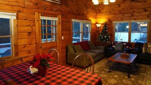 L’intérieur d’un chalet accueillant, avec un décor en bois, une table à manger recouverte d’une nappe à carreaux, un sapin de Noël et un canapé.