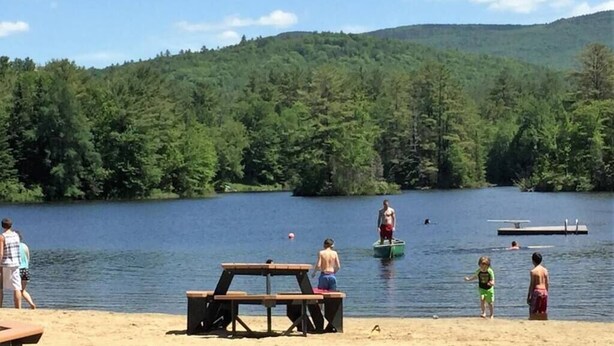 Un cadre idyllique au bord du lac, avec des tables de pique-nique, une jetée et des personnes pratiquant diverses activités nautiques.