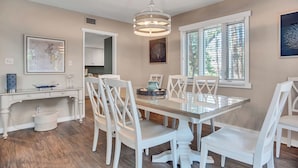 A dining area with a glass table, white chairs, a hanging light fixture, and a window with blinds. - 241 Stoney Creek at Sea Pines Resort (Hilton Head Island)