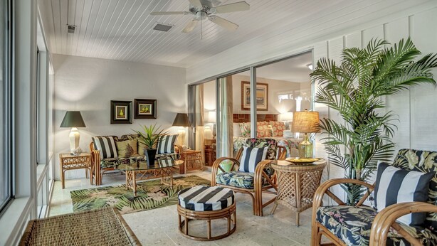 A spacious living room with wicker furniture, a ceiling fan, and a large plant.