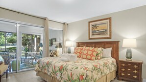 A bedroom with a bed, two bedside tables, a nightstand, a window with curtains, a door leading to a balcony, and a painting on the wall.