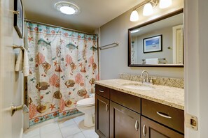 Une salle de bain avec un rideau de douche orné de motifs représentant la vie marine, un lavabo avec un plan de travail en granit et un miroir au-dessus du lavabo.