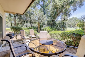 Eine Terrasse im Freien mit einem runden Glastisch und vier Stühlen, umgeben von üppiger Bepflanzung und Bäumen.