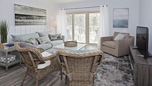 Een woonkamer met een bank, twee rieten fauteuils, een salontafel en een televisie.
