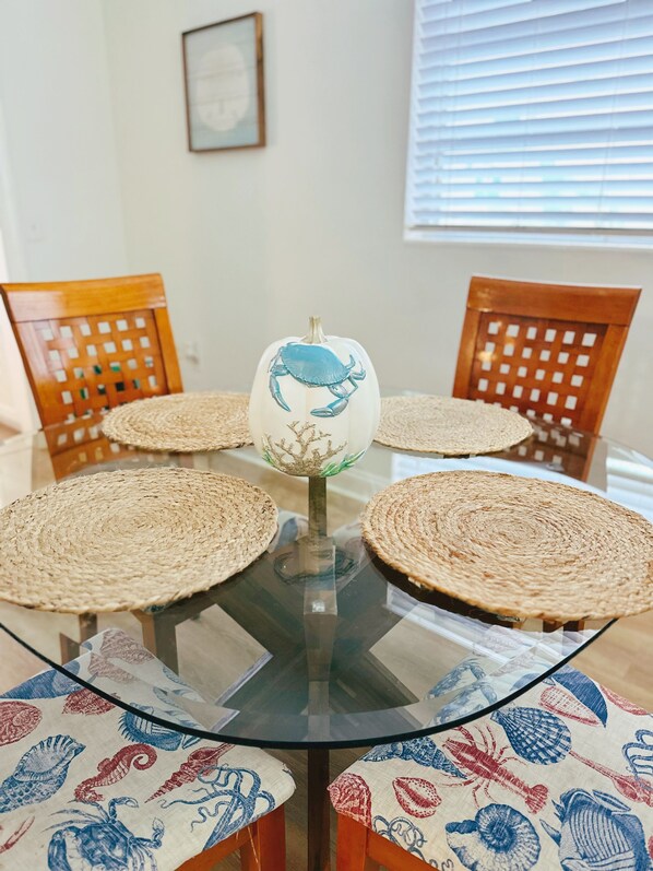 A round glass table with woven placemats and chairs with patterned cushions.