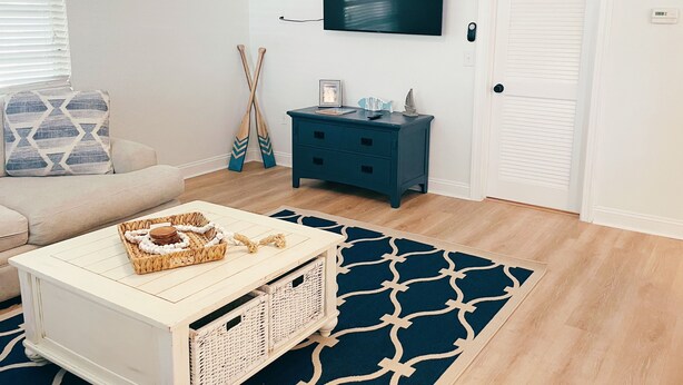 A living room with a white sofa, a blue accent wall, a TV mounted above a dark blue dresser, and a patterned rug.