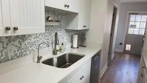 A kitchen with white cabinets, a stainless steel sink, and a tiled backsplash.