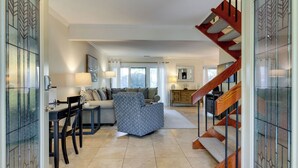 A spacious living area with a sofa, a coffee table, and a dining table with chairs. A staircase with wooden railings leads to an upper floor. - 540 Plantation Club Villas at The Sea Pines Resort (Hilton Head Island)