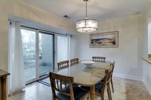 Comedor con mesa de vidrio, sillas de madera, lámpara de araña y puerta corrediza de cristal que da a un patio.