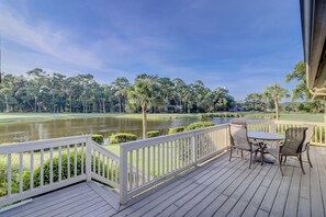 A wooden deck with a white railing, a table, and chairs overlooking a golf course and a body of water. - 552 Ocean Course at Sea Pines Resort (Hilton Head Island)