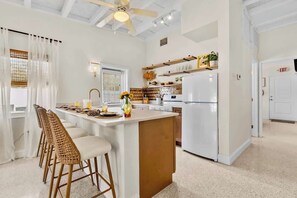 A modern kitchen with a central island, bar stools, and a ceiling fan.