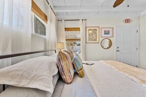 A bedroom with a bed, pillows, a window with curtains, a door with an exit sign, and framed pictures on the wall.