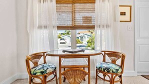 A round table with four wicker chairs, a glass top, and sheer curtains.