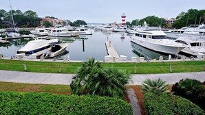 A marina with multiple boats docked, a lighthouse in the background, and a grassy area with plants in the foreground. - 838 Ketch Court at The Sea Pines Resort (Hilton Head Island)