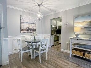 A dining area with a round table, white chairs, a chandelier, and a painting of a bicycle on the wall. - 870 Ketch Court at The Sea Pines Resort (Hilton Head Island)