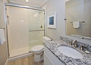 Un bagno moderno con doccia vetrata, un water bianco, un lavabo con piano in granito e uno specchio grande.