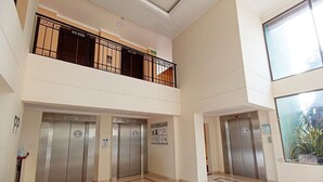 Un hall d’entrée spacieux avec deux ascenseurs, un balcon doté d’une rambarde en métal et une grande fenêtre sur le côté droit.