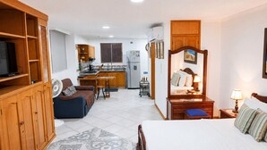 Une chambre d’hôtel de taille réduite, comprenant un lit, un petit bureau, un canapé, une kitchenette et un téléviseur.