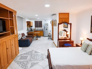 Quarto de hotel compacto com uma cama, uma pequena escrivaninha, um sofá, uma cozinha compacta e uma televisão.