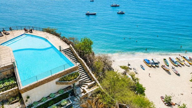 Une piscine située à côté d’une plage, avec des bateaux et un escalier menant à l’eau.