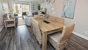A dining area with a wooden table and wicker chairs, a chandelier, and a painting of a bird on the wall. - 904 Cutter Court at Sea Pines Resort (Hilton Head Island)