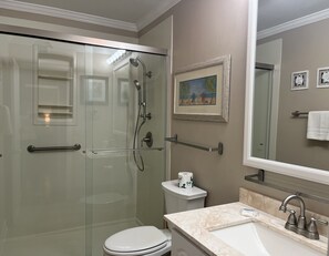 Une salle de bain dotée d’une douche à parois de verre, de toilettes, d’un lavabo avec un plan de travail en marbre et d’un tableau encadré au mur.