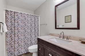 Ein Badezimmer mit Duschvorhang, Toilette, Waschbecken mit Spiegel und Handtuchhalter.