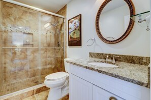 Un bagno con doccia vetrata, un water bianco, un lavabo con piano in granito e uno specchio grande con cornice decorativa.