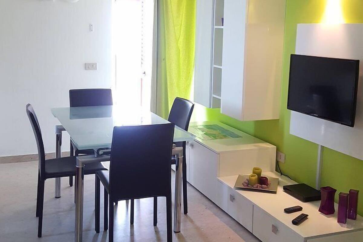 A modern living room with a dining table, chairs, a TV, and a green accent wall.