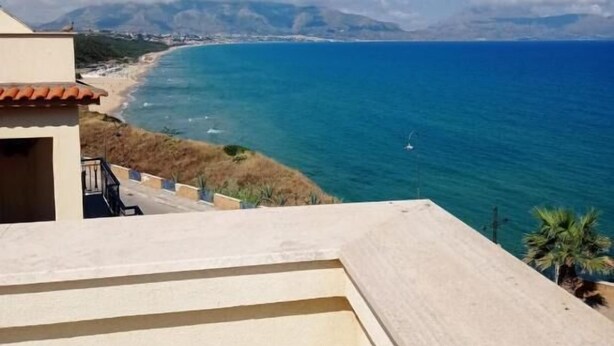 Blick auf die Küste vom Balkon mit Blick auf einen Strand, klares blaues Wasser und entfernte Berge.