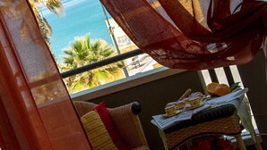 Ein Zimmer mit Meerblick, ein Korbstuhl und ein Tisch mit Korb und Buch.