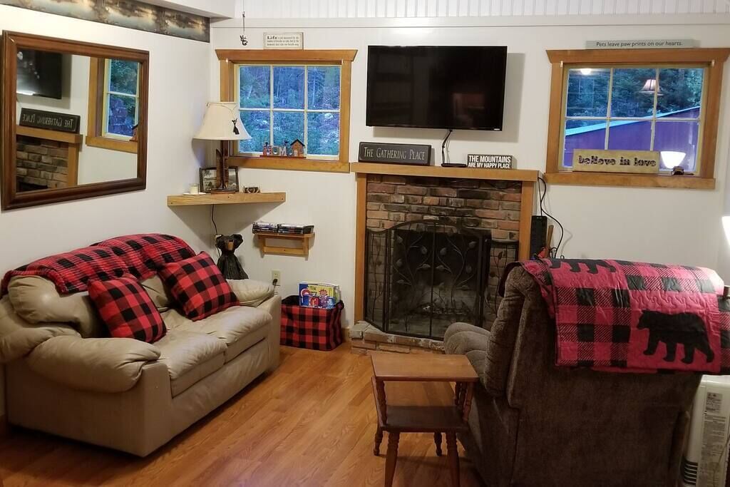 Ein gemütliches Wohnzimmer mit Kamin, einem darüber hängenden Fernseher und einem Fenster mit Blick auf eine verschneite Landschaft.
